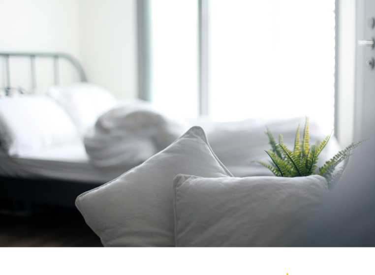 Allergievriendelijk beddengoed met witte kussens en een dekbed in een lichte, minimalistische hotelkamer.