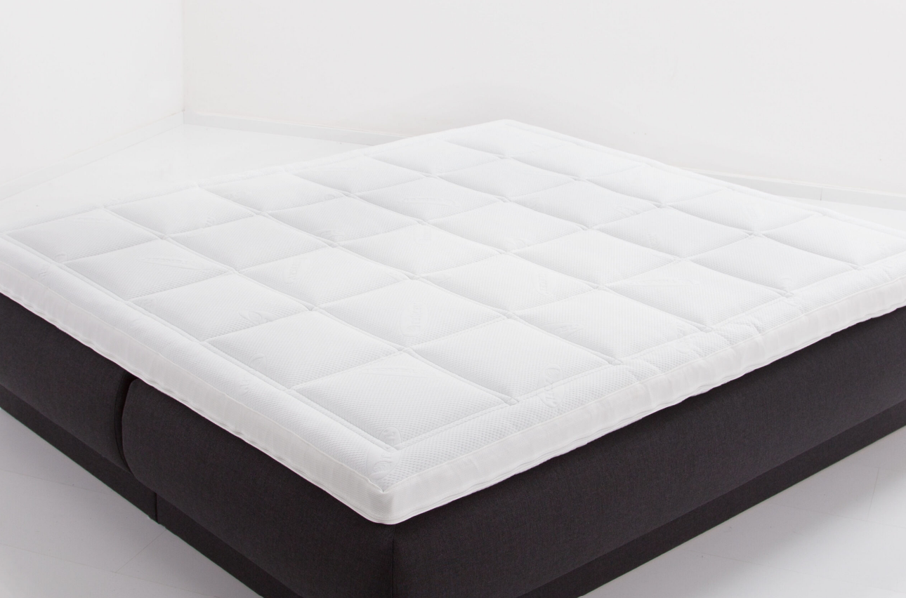 Een luxe witte matras topper of bodytop op een donkere boxspringbasis in een studio-opstelling.